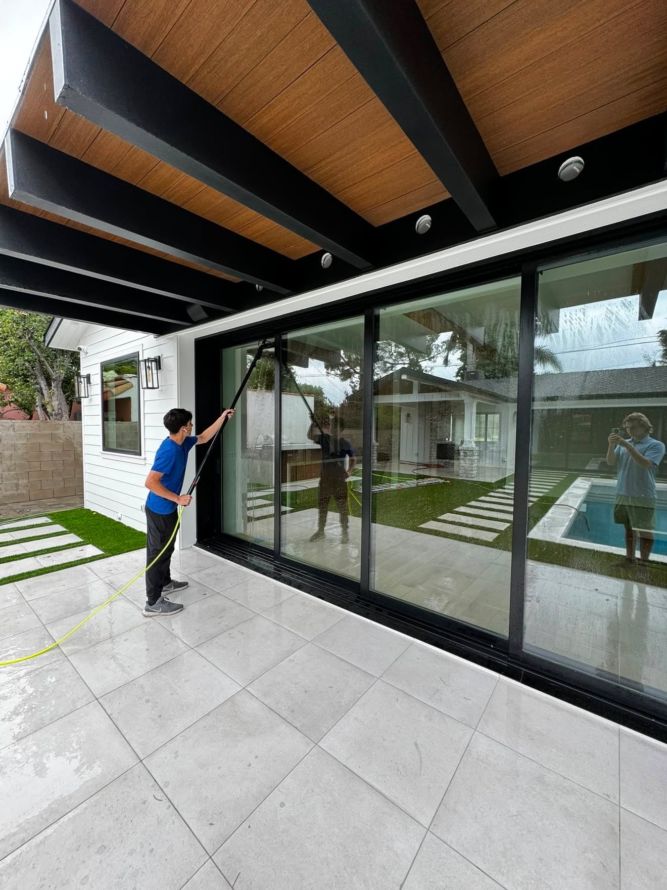Technician washing tall sliding glass doors with a water-fed pole