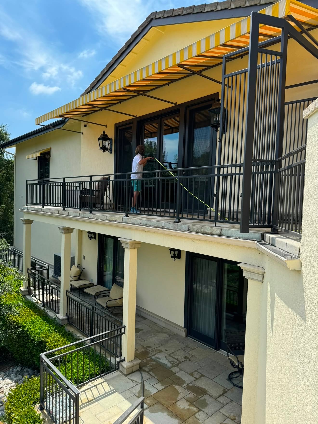 Technician cleaning upper balcony glass doors with a water-fed pole
